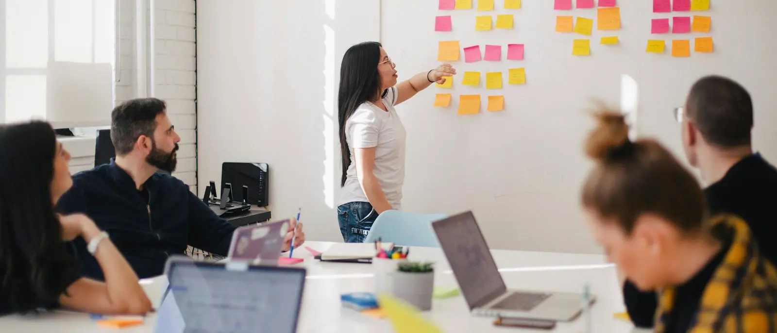 Equipe planejando em frente a um painel de notas adesivas, com laptops sobre a mesa