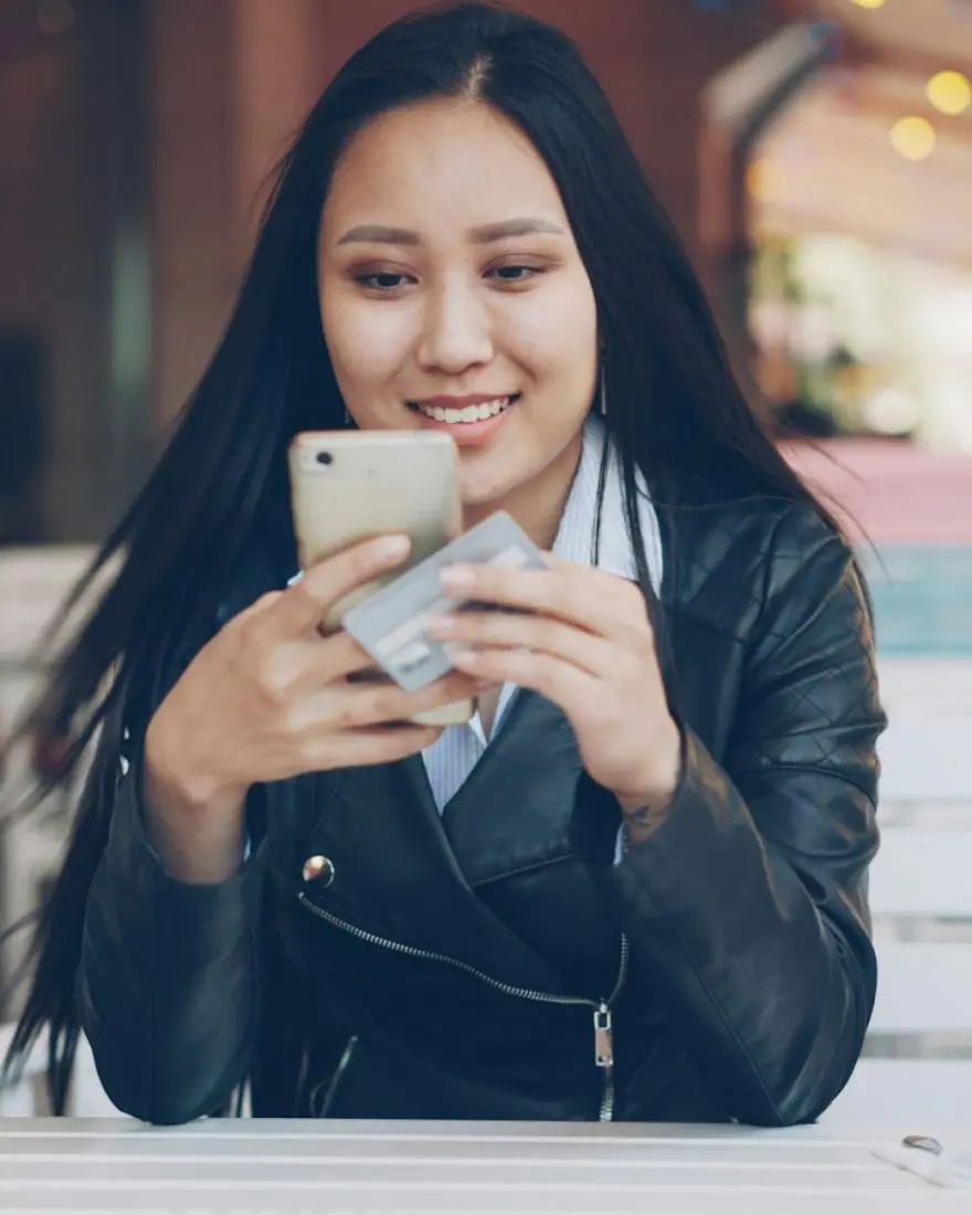 Mulher sorrindo enquanto usa o celular numa mesa de café