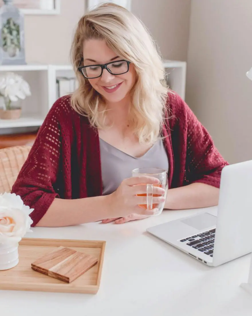 Mulher de óculos sorrindo em frente ao laptop, numa mesa clara de escritório